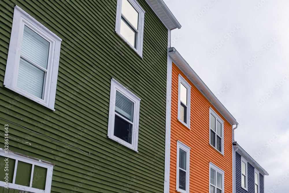 A street view of multiple colorful wooden homes with double hung windows. The closed glass windows have white trim. There's a green, orange and blue house with cloudy sky in the background.  