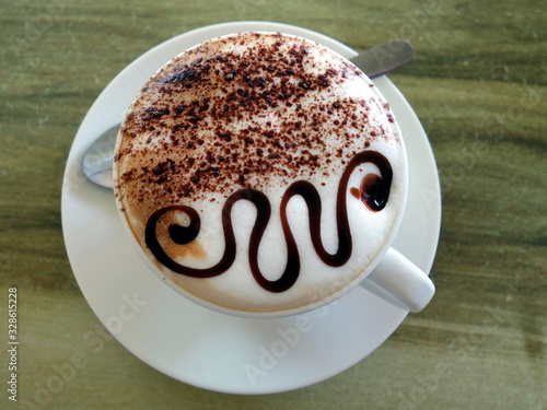 A cup of Cappuccino showing a very clever chocolate design on top.