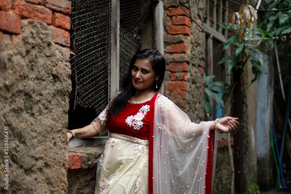 Portrait of an young and attractive Indian Bengali brunette woman standing in front of a vintage brick wall wearing Indian traditional ethnic cloths. Indian lifestyle and fashion