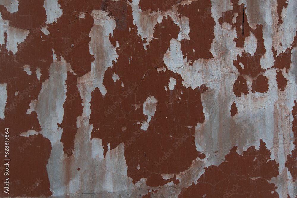 Old weathered painted wall background texture. Red dirty peeled plaster wall with falling off flakes of paint.Peeling paint on a metal surface.Cracked paint damaged concrete rough texture.