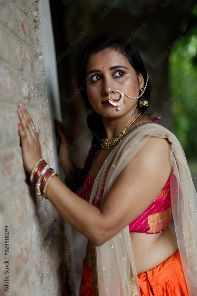 Portrait of an Young and beautiful Indian Bengali brunette woman standing while holding a brick wall wearing Indian traditional ethnic vibrant skirt blouse. Indian lifestyle and fashion Portrait of an Young and beautiful Indian Bengali brunette woman standing while holding a brick wall wearing Indian traditional ethnic vibrant skirt blouse. Indian lifestyle and fashion