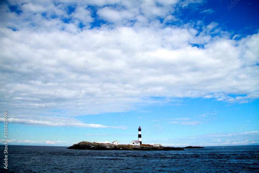 Race Rocks lighthouse and island in the Salish Sea set in a sunny day with white fluffy clouds.