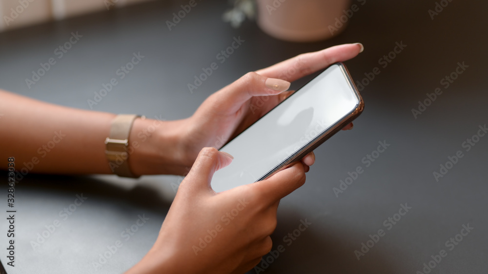 Cropped shot of college girl typing on mock-up smartphone on black table Cropped shot of college girl typing on mock-up smartphone on black table