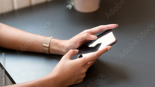 Cropped shot of college girl typing on smartphone on black table in coffee shop