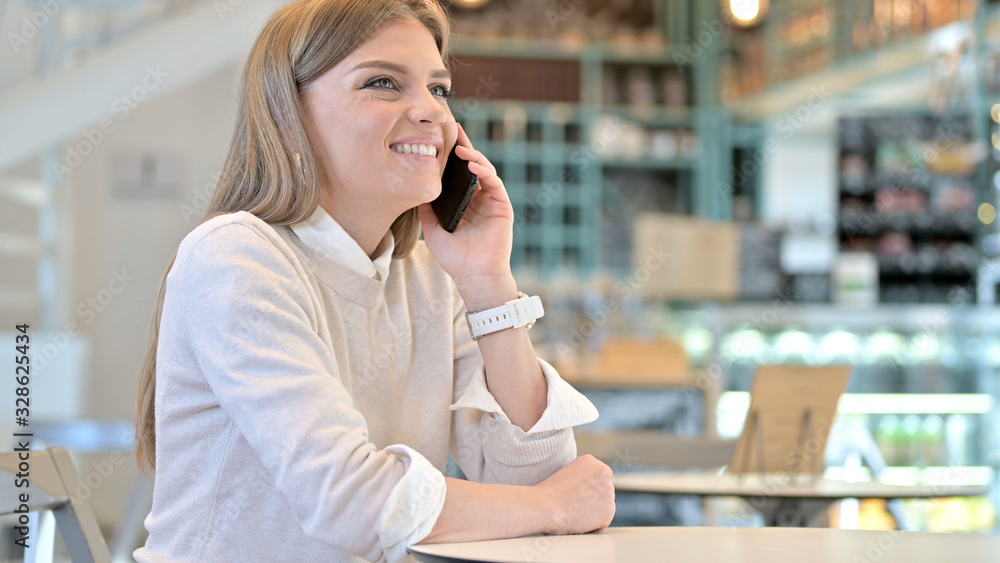 Cheerful Young Woman Talking on Smartphone in Cafe