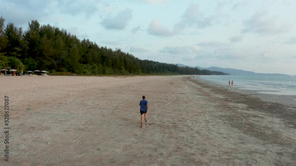Tracking shot of a male runner on a tropical beach at sunset Tracking shot of a male runner on a tropical beach at sunset