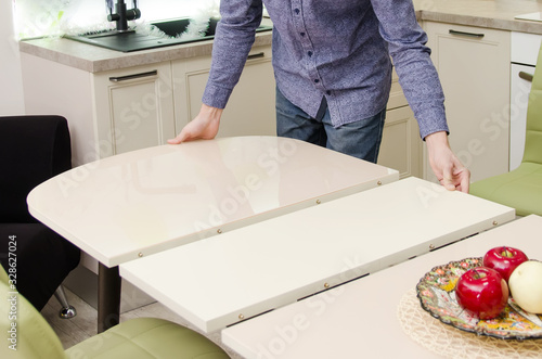 man lays out a sliding glossy dining table on which stands a plate with artificial fruit