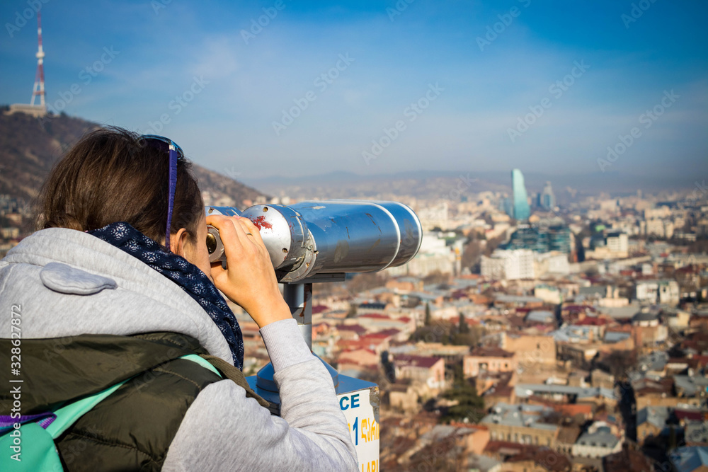Girl watching Tbilisi city sightseeing view over binoculars or telescope