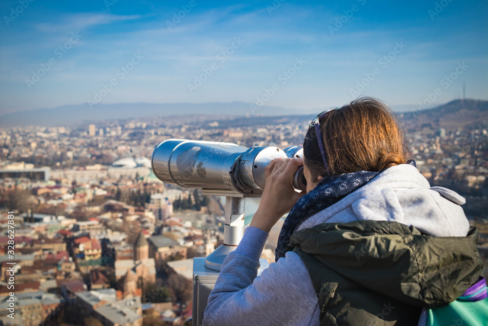 Girl watching Tbilisi city sightseeing view over binoculars or telescope