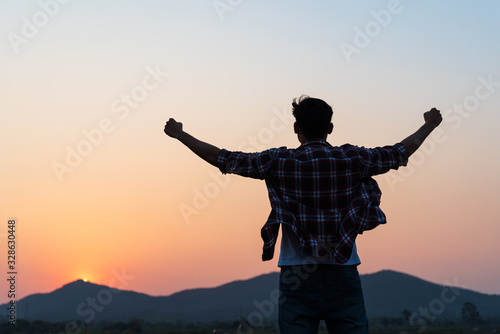 Man with fist in the air during sunset sunrise mountain in background. Stand strong. Feeling motivated, freedom, strength and courage concept. photo