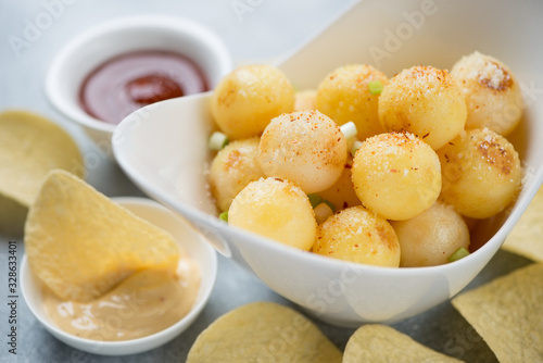 Closeup of a white bowl with roasted potato balls and dipping sauces, selective focus