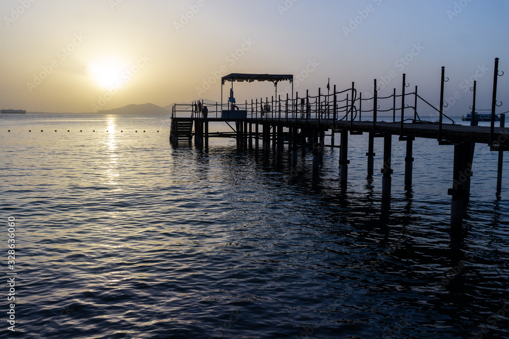 Sea raft in the sun rising on the shore of an Egyptian beach with a long wooden platform that goes deep into the water. Golden rays of the sun on the sea or ocean surface of calm water.