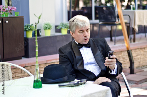 A grey-haired elderly mobster sitting in a summer cafe. photo