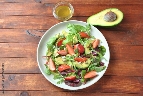 Avocado salad with strawberries, blue cheese, arugula and beet leaves on wooden background. Healthy lunch bowl Vegan healthy food concept