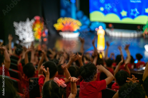 Children excitingly raise hands watching the performance in the theater