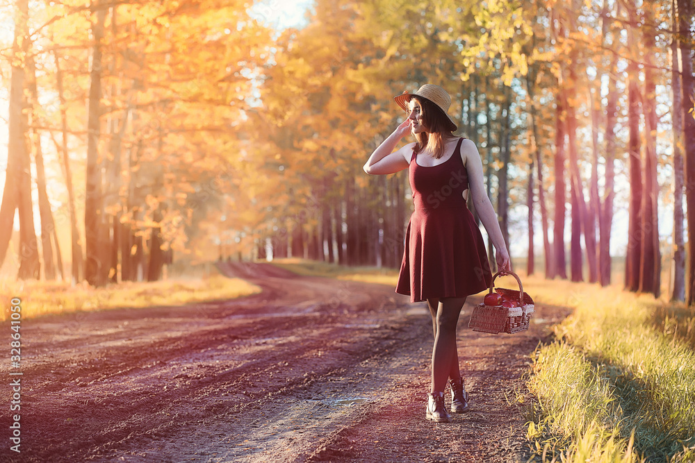 A girl in a hat on a walk in the park. A girl with a basket walks in autumn. A girl is walking along the road at sunset.