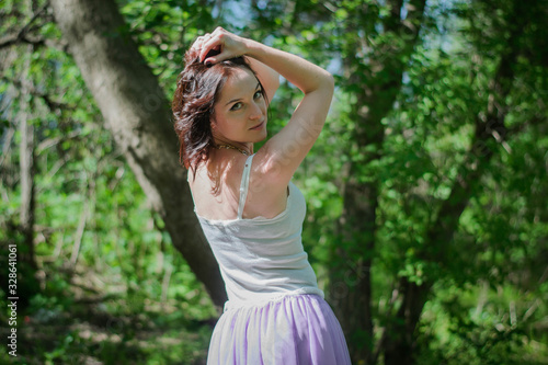 Beautiful young brunette woman posing in a forest among shrubs and trees