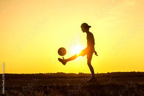 Boy playing with ball in nature in hot evening, silhouette of playing child at sunset in countryside
