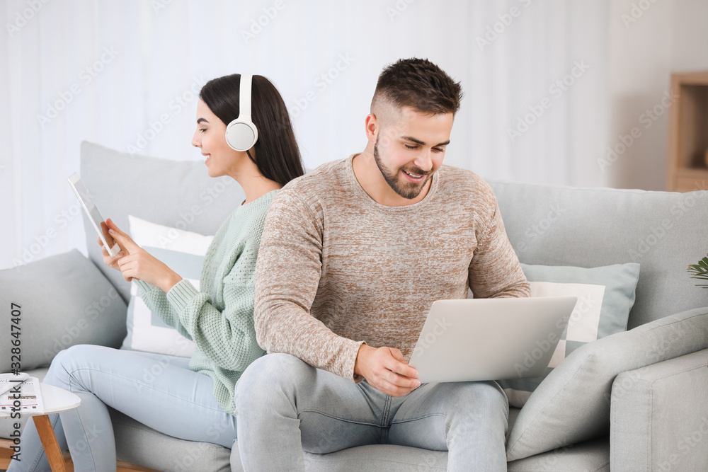 Young couple with modern devices resting on sofa at home Young couple with modern devices resting on sofa at home