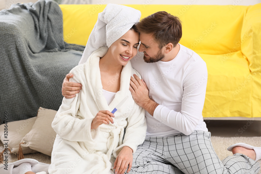 Fototapeta premium Happy young couple with pregnancy test at home