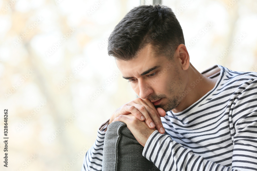 Depressed young man near window at home Depressed young man near window at home