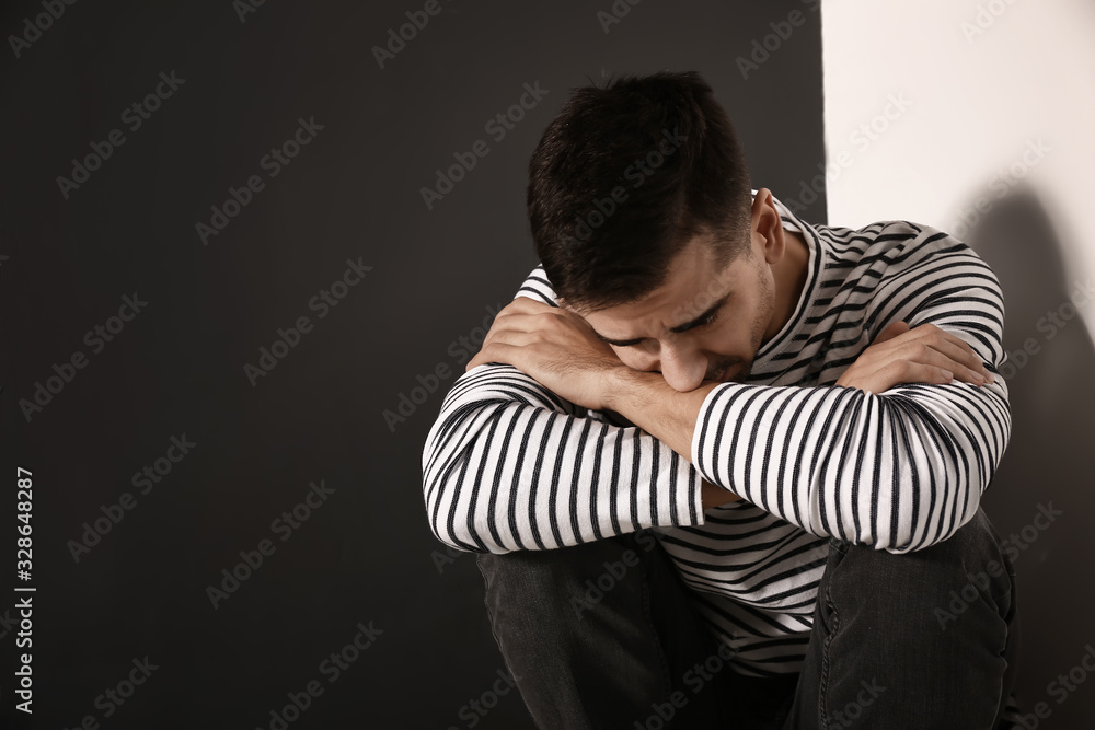Depressed young man sitting near wall Depressed young man sitting near wall