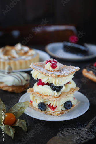 Tea and sweets on a dark background  Mille-feuille  Eclairs  Tart  Decorative with flowers  Selective focus  Closeup