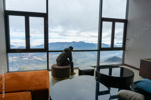 Hotel room with mountain landscape view from window  interiors with chairs and table  and a man sits seeing the scene through window