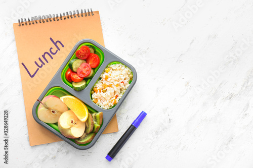 School lunch box with tasty food and notebook on light background
