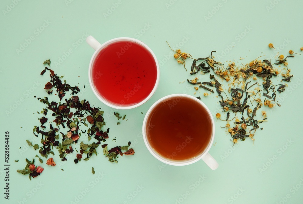 Cups with fruit and herbal tea, dried herbs, healthy drink, herbal medicine, flat lay on green background.