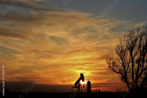 Kansas colorful Sunset clouds and an Oilwell Pump with tree's out in the country.