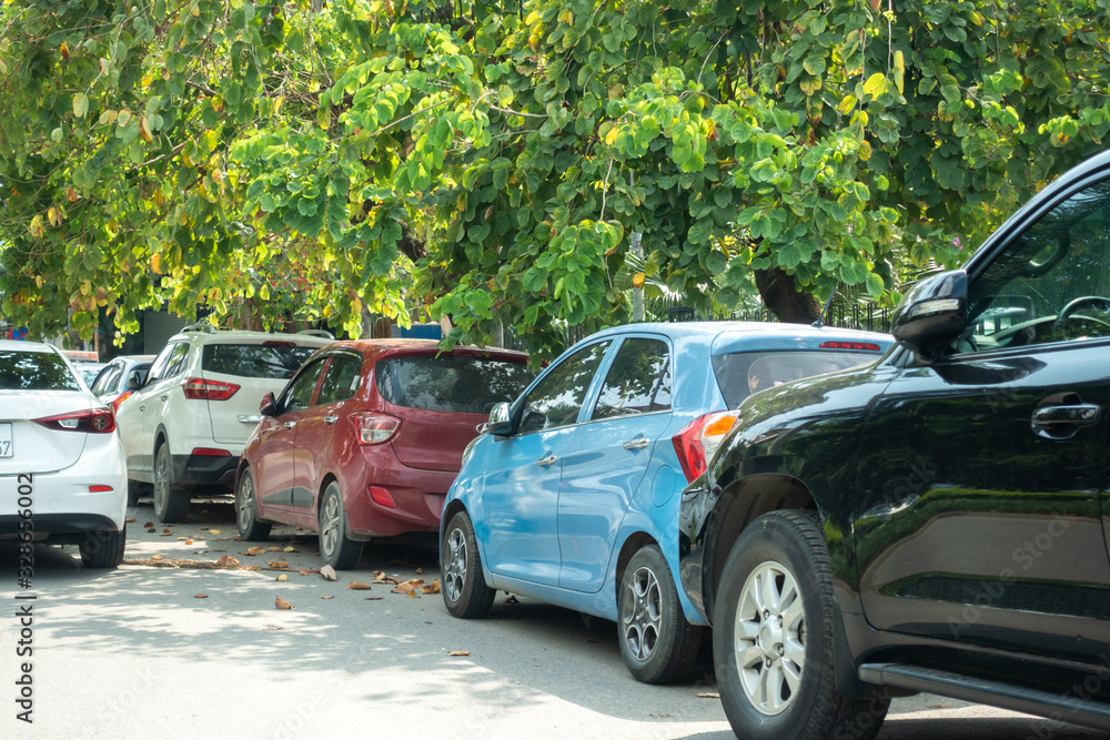 Parallel cars parking on street with green trees