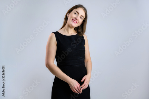 Generic concept of a pretty Caucasian woman. A model stands in front of the camera with a smile in a black dress on a white background. © Вячеслав Чичаев