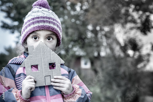 The girl is five years old. She is holding a house cut out of cardboard.