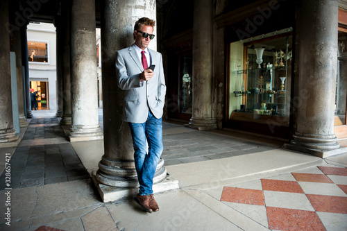Cuadro en lienzo Well dressed man using his mobile phone leaning against a column on the classic