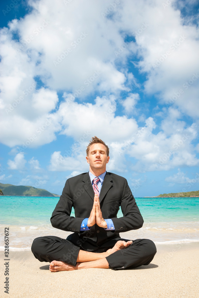 Meditating businessman sitting barefoot in his suit with namaste hands in a cross-legged easy yoga pose on the shore of a sunny tropical beach Meditating businessman sitting barefoot in his suit with namaste hands in a cross-legged easy yoga pose on the shore of a sunny tropical beach