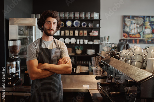 Male business owner behind the counter of a coffee shop with folded hands looking at camera