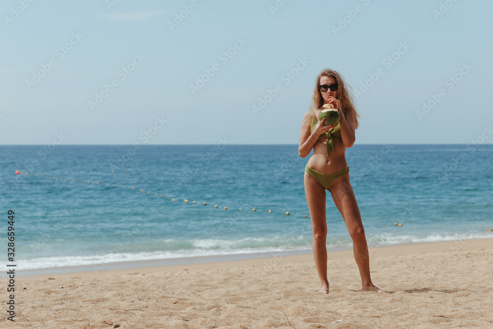 The girl with the coconut on the beach. Girl drinks coconut milk on the beach. High quality photo