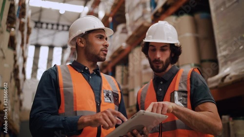 Diverse young male workers discussing and using digital tablet while supervising production at distribution warehouse