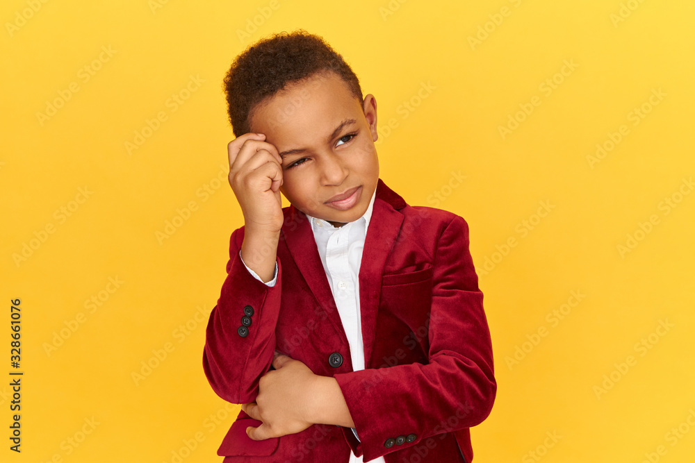 Pensive adorable little boy of African appearance looking upward keeping hand on his forehead having thoughtful facial expression, trying to recollect important information. Thoughts and ideas Pensive adorable little boy of African appearance looking upward keeping hand on his forehead having thoughtful facial expression, trying to recollect important information. Thoughts and ideas