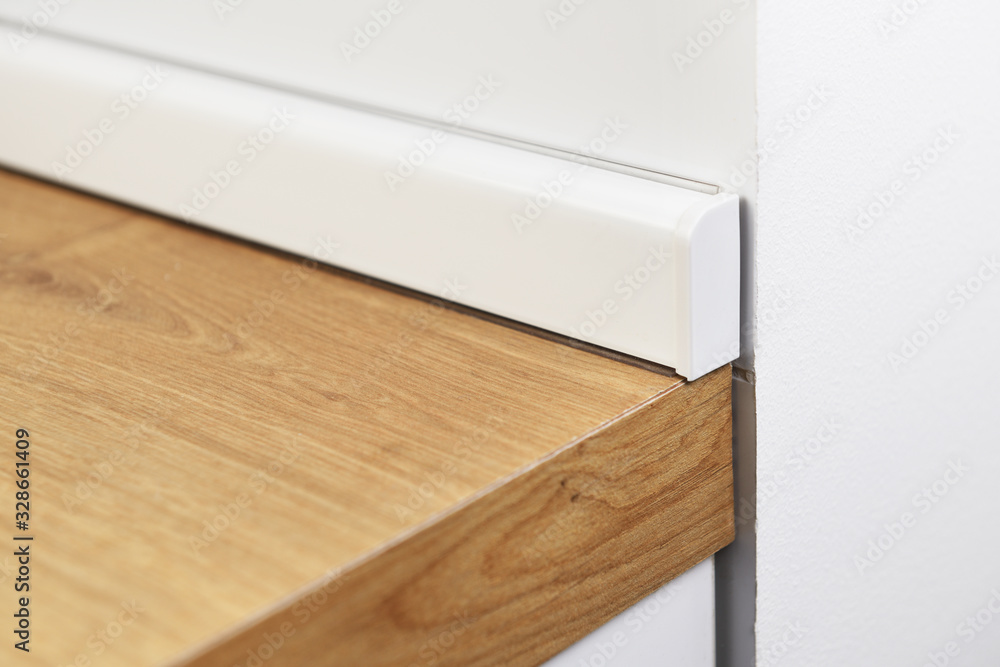 Wood corner kitchen worktop with white plastic baseboard.The corner of