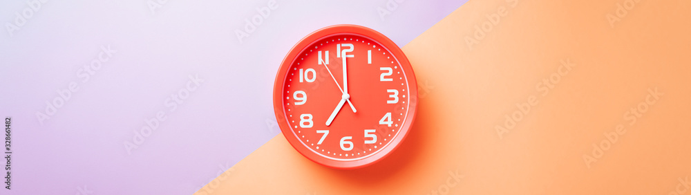 Red clock alarm clock on colored background divided into lilac and beige color web banner: planning or working time concept Red clock alarm clock on colored background divided into lilac and beige color web banner: planning or working time concept