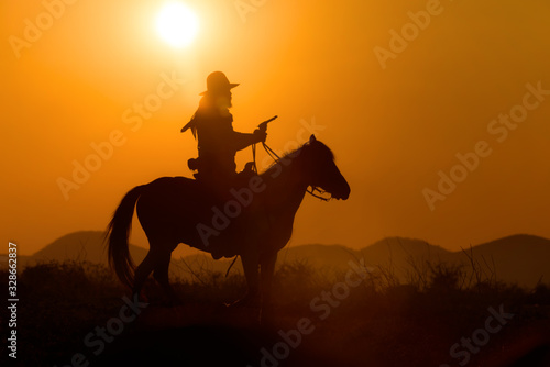 Cowboy riding a horse carrying a gun in sunset with mountain 