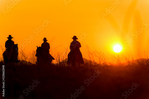 Cowboy riding a horse carrying a gun in sunset with mountain  © weerachai