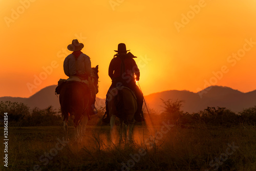 Cowboy riding a horse carrying a gun in sunset with mountain 