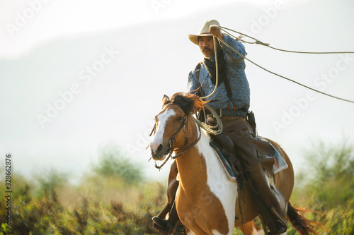  A western cowboy riding a horse in a hand holding a rope © weerachai