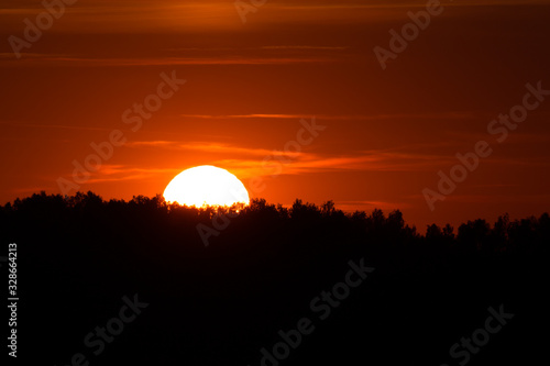 Part of the setting sun behind forest silhouette