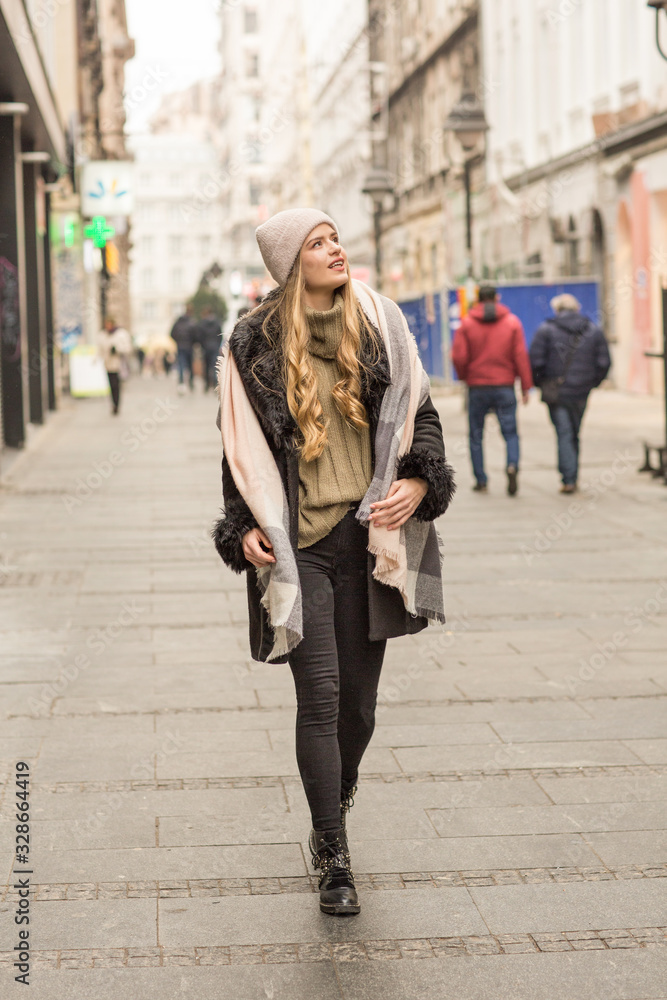 Beautiful young woman in winter autumn outfit walking in the city street