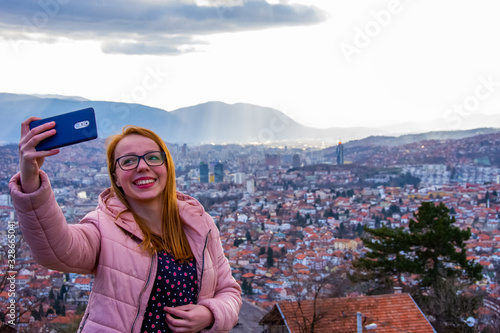 Girl with glasess and brown hair taking selfie above Sarajevo with mobile phone photo