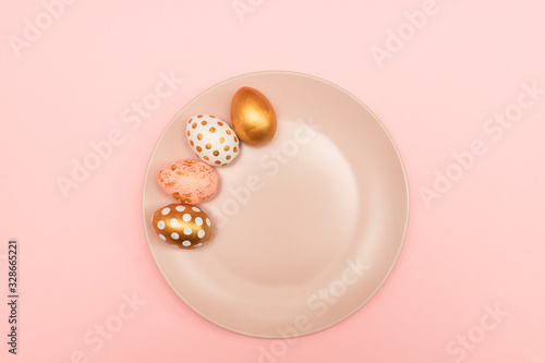 Top view of pink, white and golden decorated eeaster eggs on pink plate on pink background. Trendy holiday backdrop photo